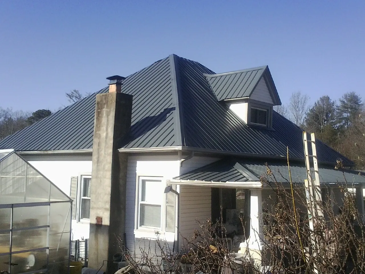 Dark blue standing seam metal roof on a white farmhouse with dormer — Slate & Tile Roof Repair by Roofing Brothers in Kendall Park