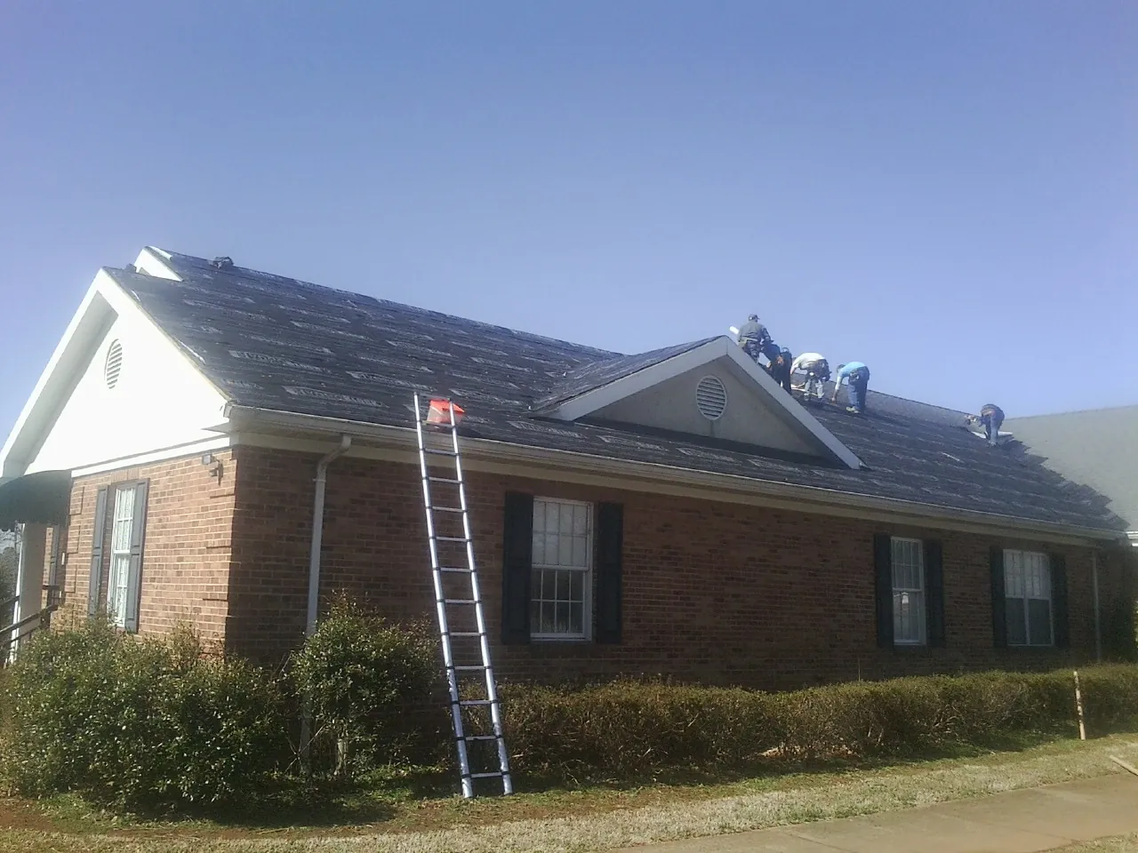 Crew tearing shingles off a brick ranch roof with a ladder set — Emergency Roof Repair work by our crew in Kendall Park