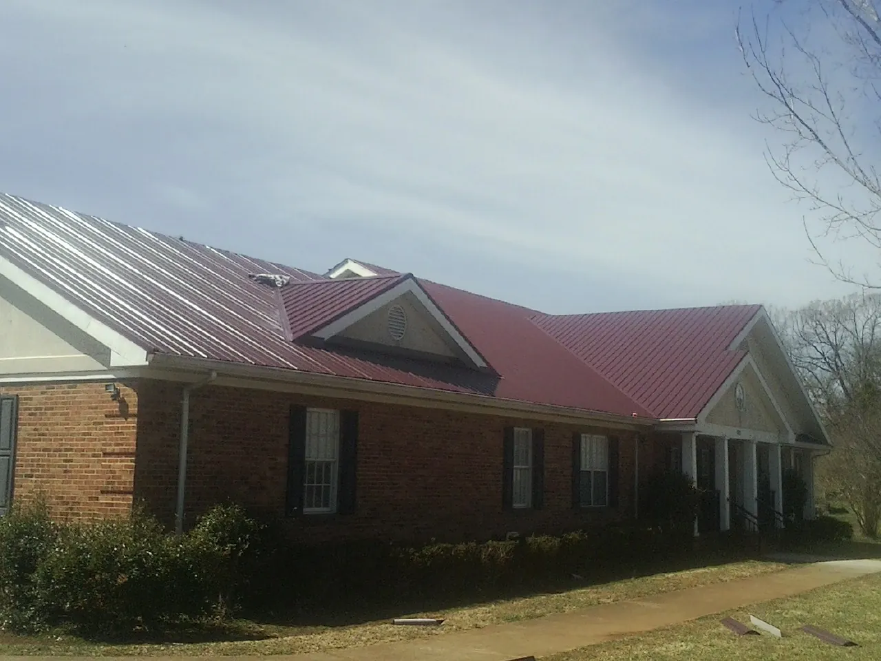 Red metal roof with gabled entries on a long brick building, from a Hail Damage Roof Repair job in Kendall Park