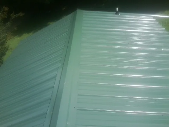 New green metal panels meeting at the ridge of a roof — Flat Roof Repair work by our crew in Kendall Park