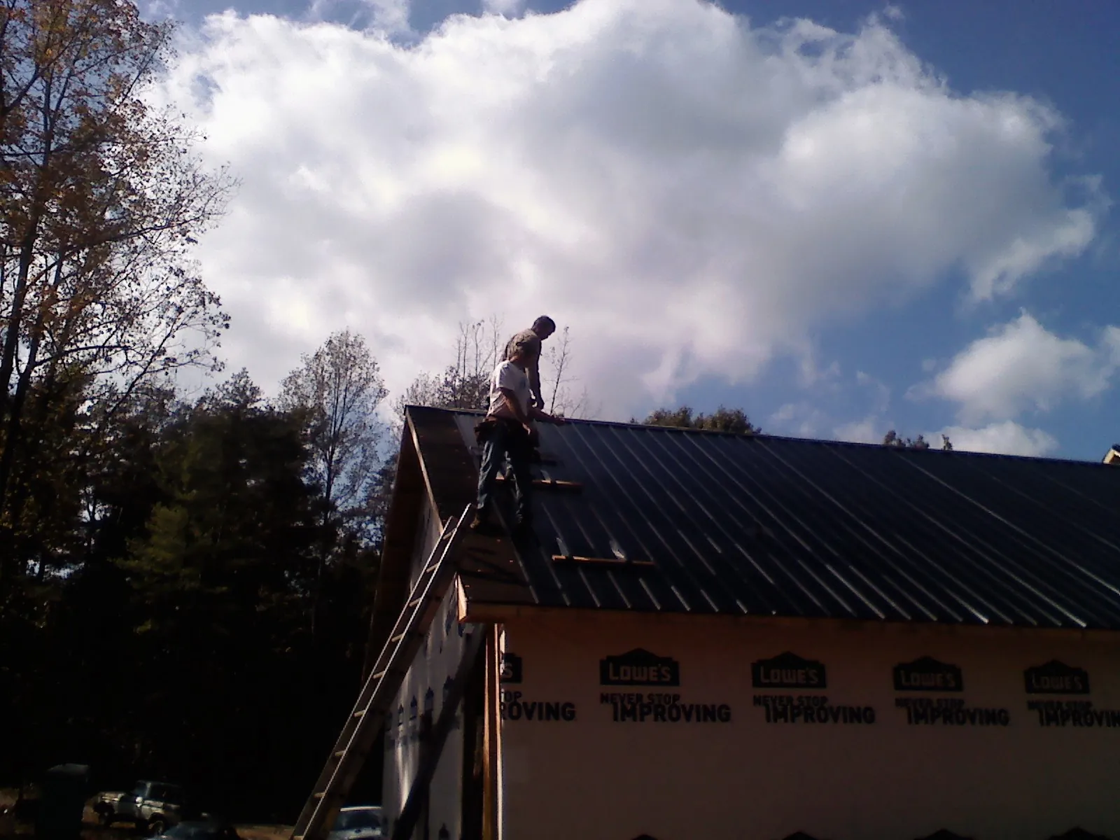 Roofer fastening dark metal panels high against a cloudy sky, from a Roof Inspection job in Kendall Park