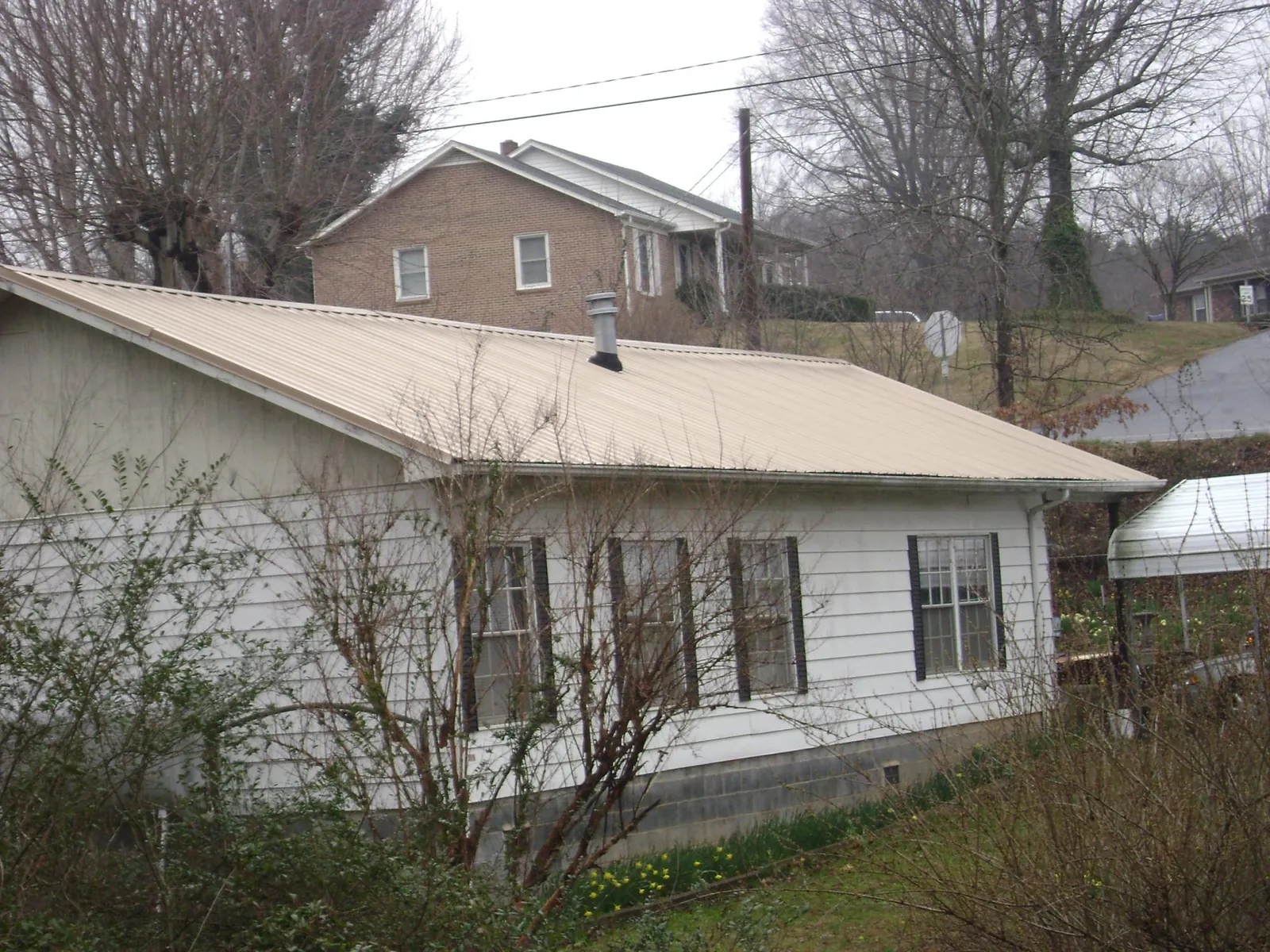 Tan metal roof on a white sided house set into a hillside — Commercial Roofing by Roofing Brothers in Kendall Park